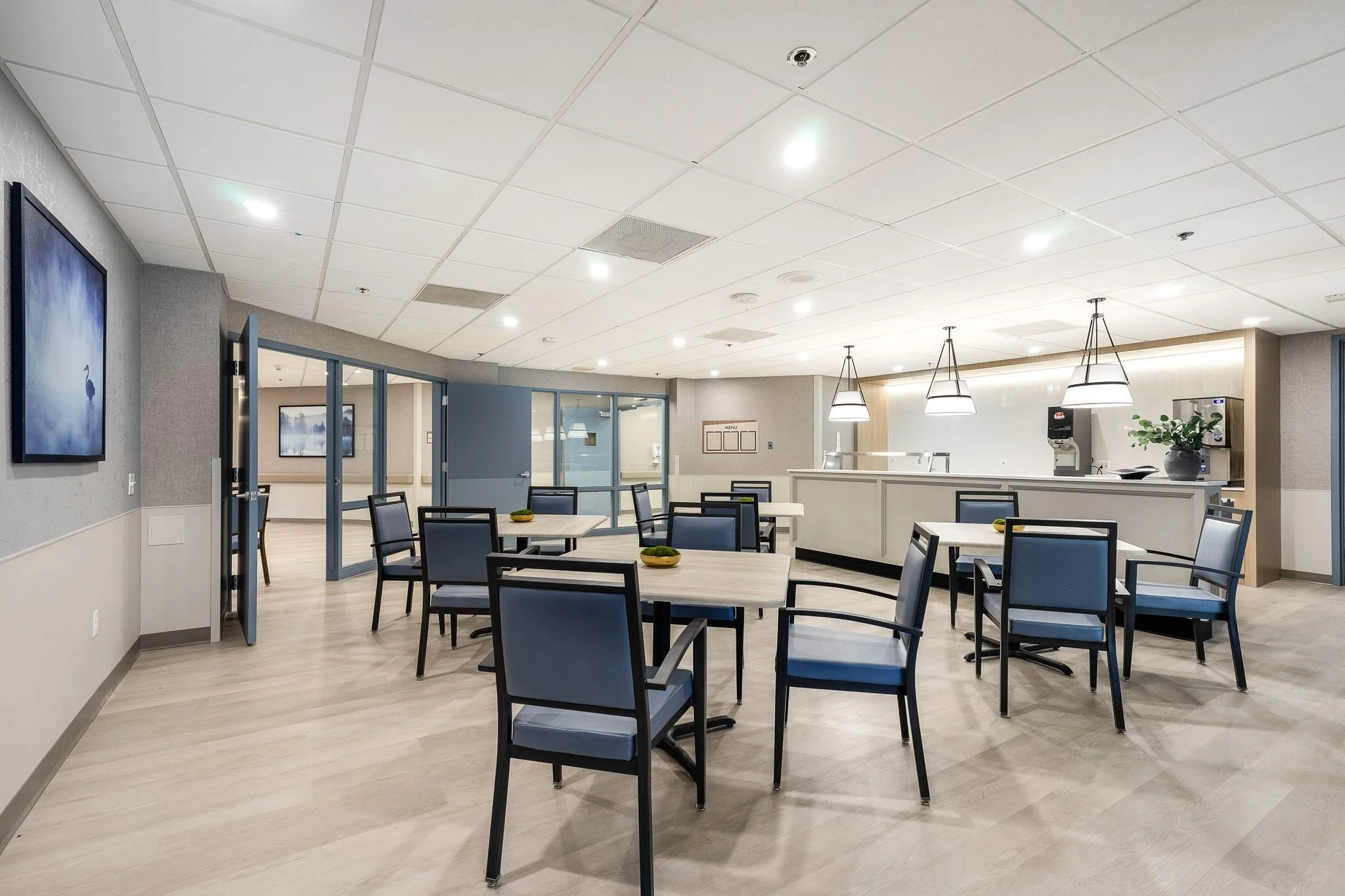 Empty indoor dining area with tables and chairs, ceiling lights, and artwork on the walls.
