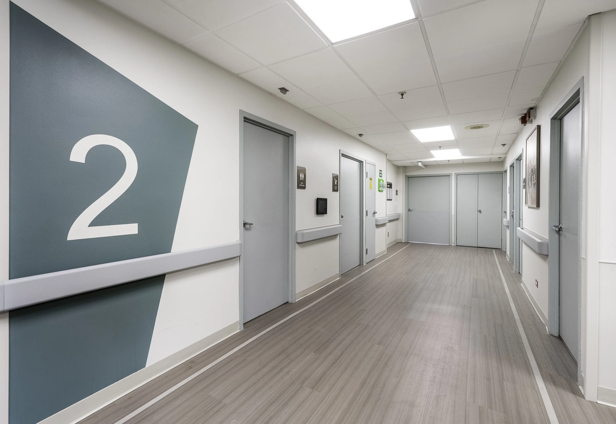 Hospital hallway with multiple patient rooms, bathroom icons, and an emergency exit sign.