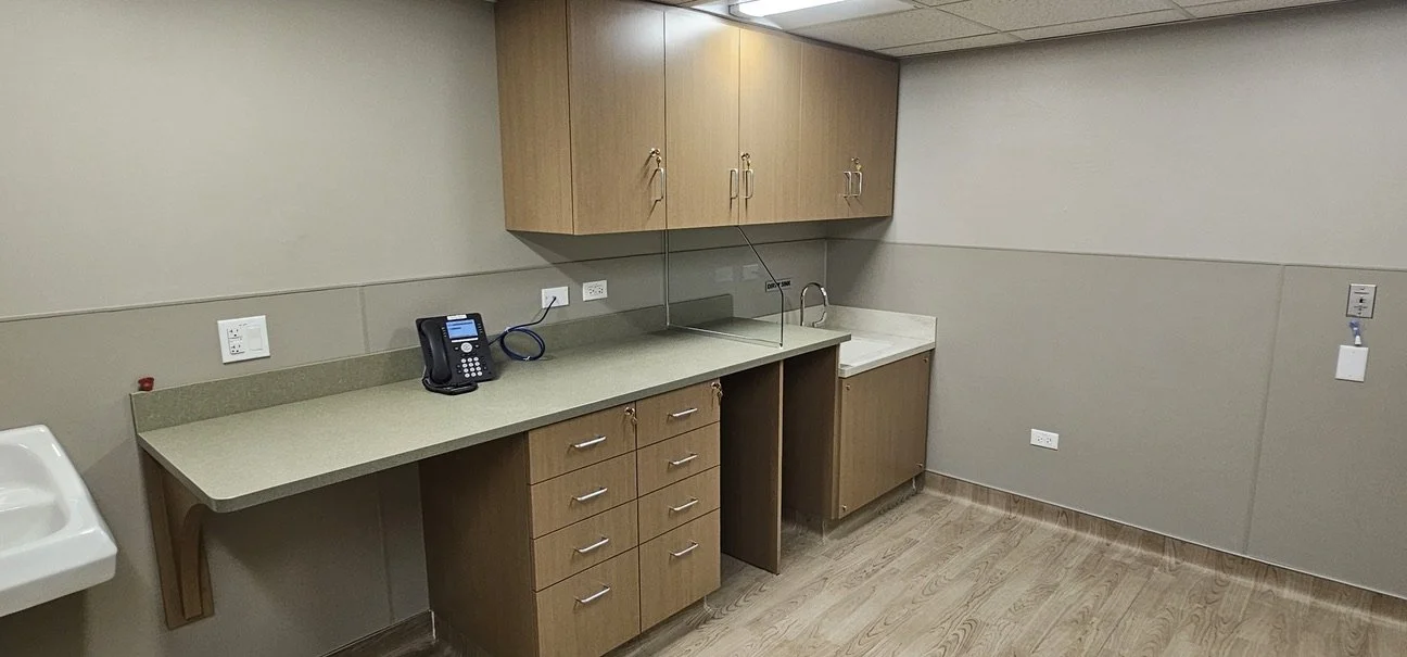 Empty medical examination room with a countertop, cabinets, a sink, and a phone.
