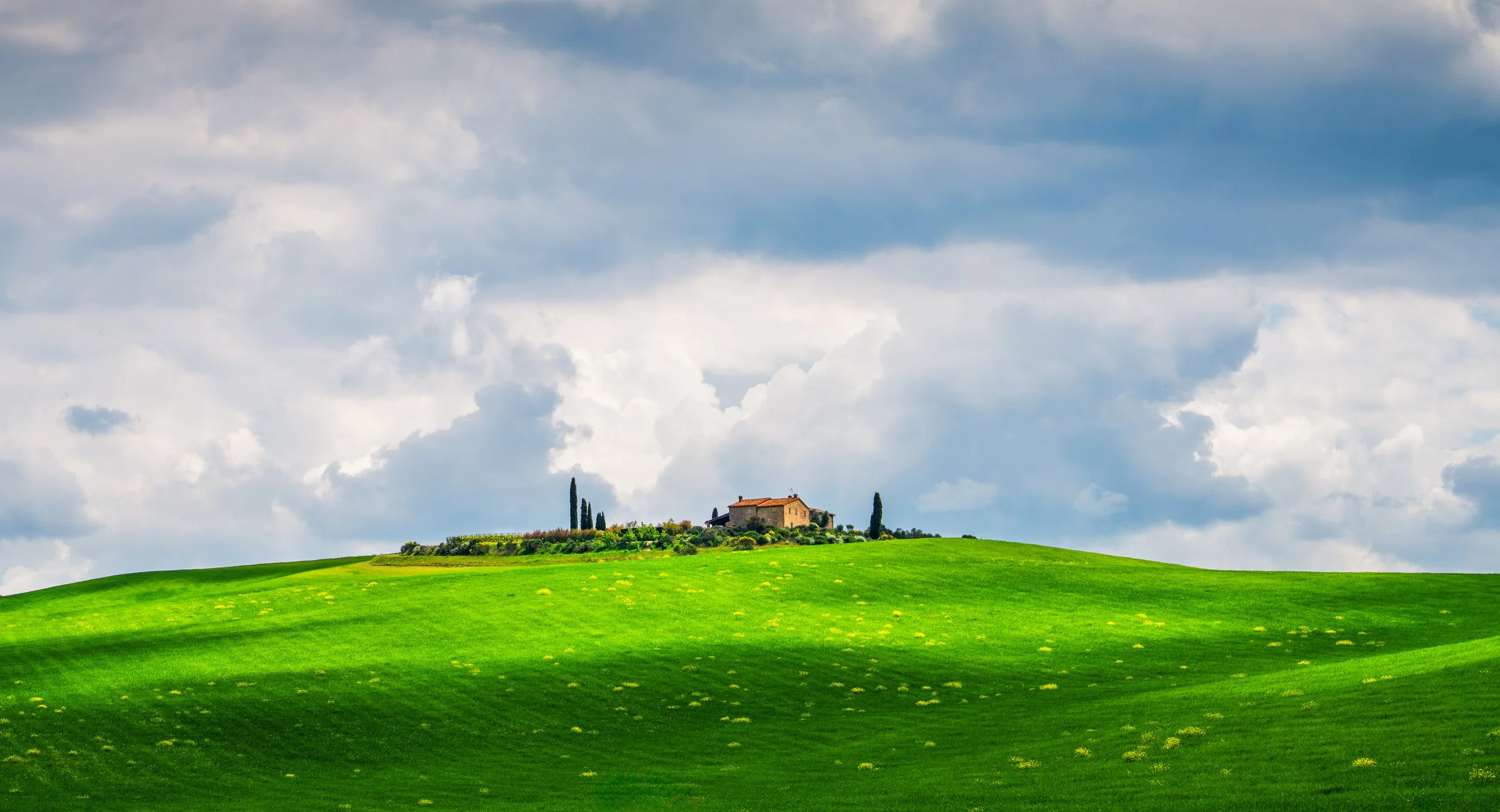 Beautiful view of a traditional Tuscan farmhouse set on rolling green hills, surrounded by cypress trees under a dramatic cloudy sky. A classic Italian countryside scene that captures the charm and tranquility of Tuscany, perfect for travel inspirati