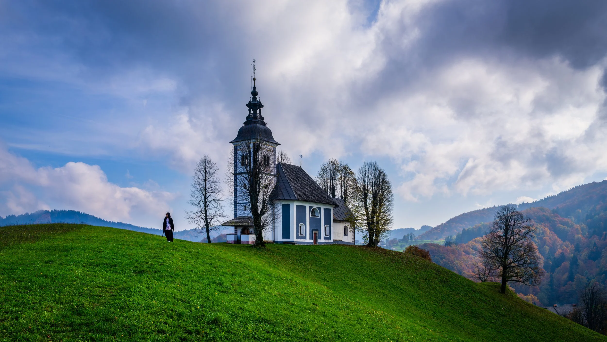 Picturesque hilltop church surrounded by lush green meadows and misty Slovenian mountains near Škofja Loka, perfect for scenic travel and photography in the countryside.