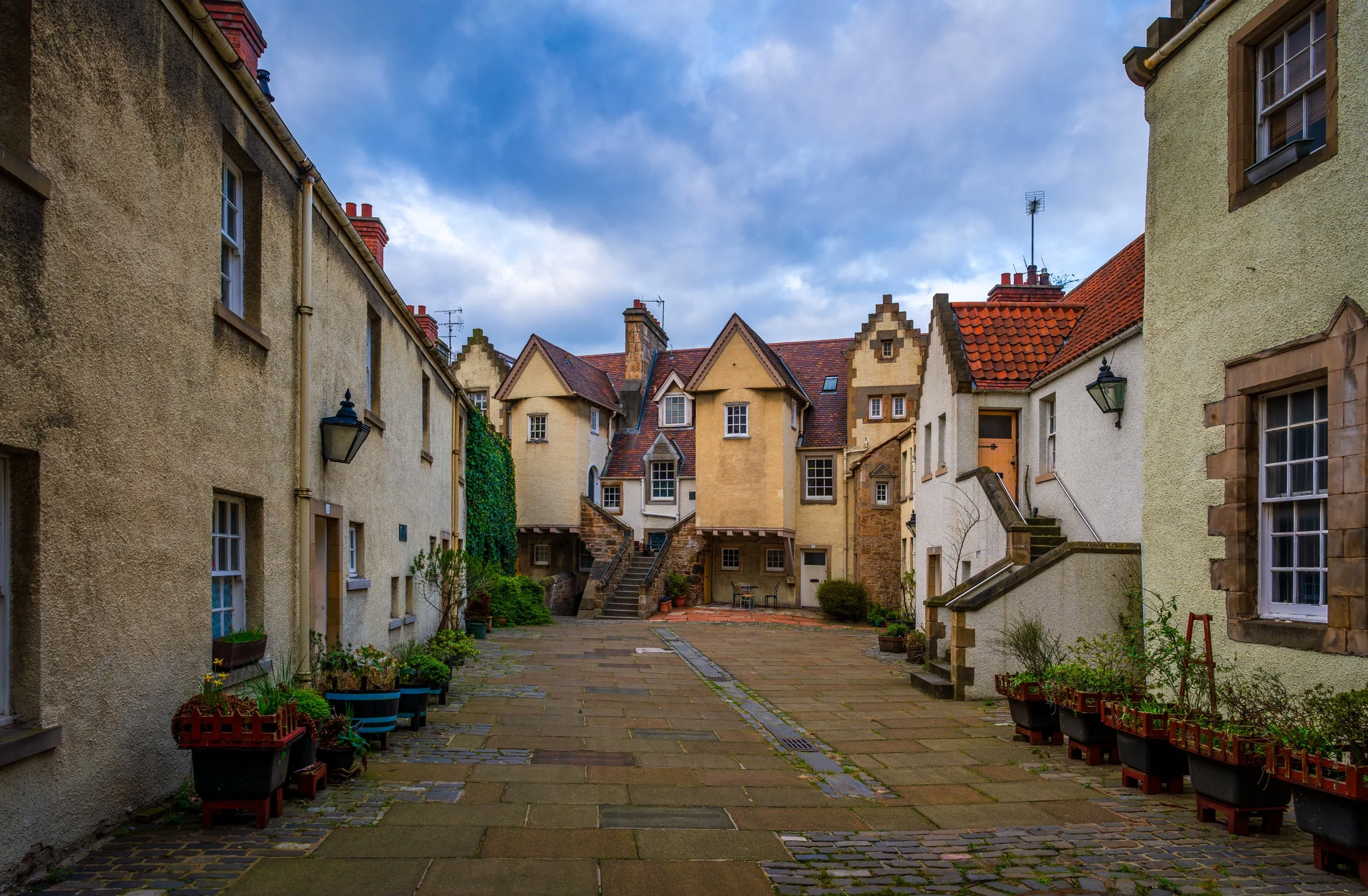 Historic courtyard in Edinburgh, Scotland, surrounded by traditional stone houses and distinctive Scottish architecture under a dramatic cloudy sky.