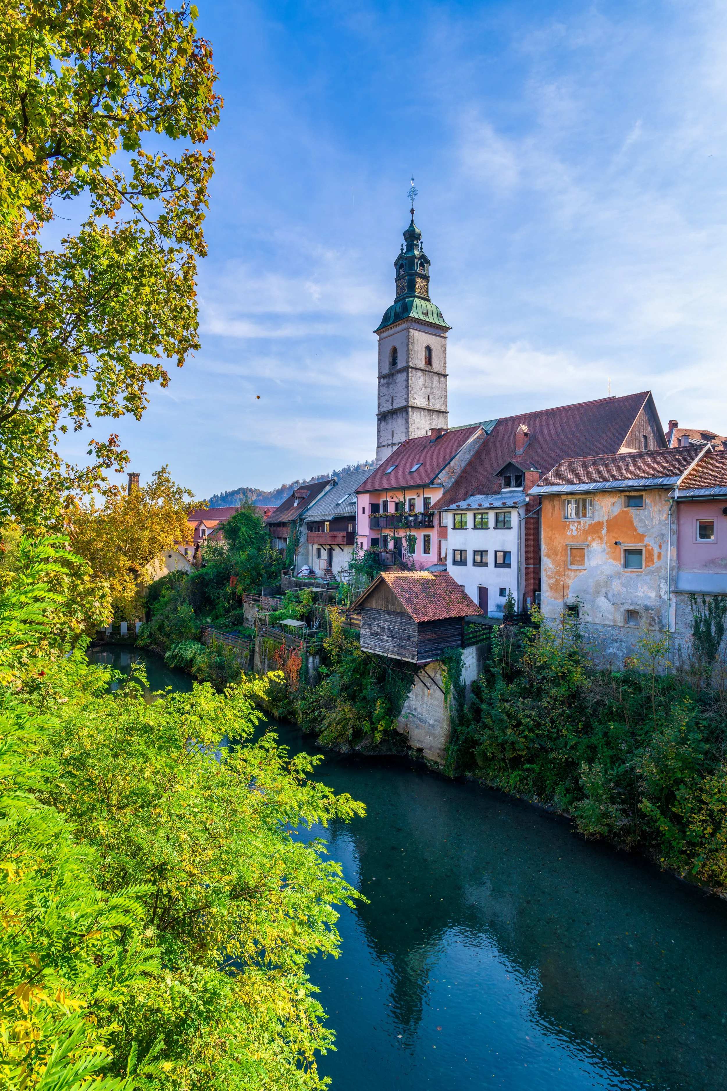 Historic riverside view of Škofja Loka old town with the St. Jacob’s Church tower and colorful medieval houses reflecting in the Selca Sora River, Slovenia.