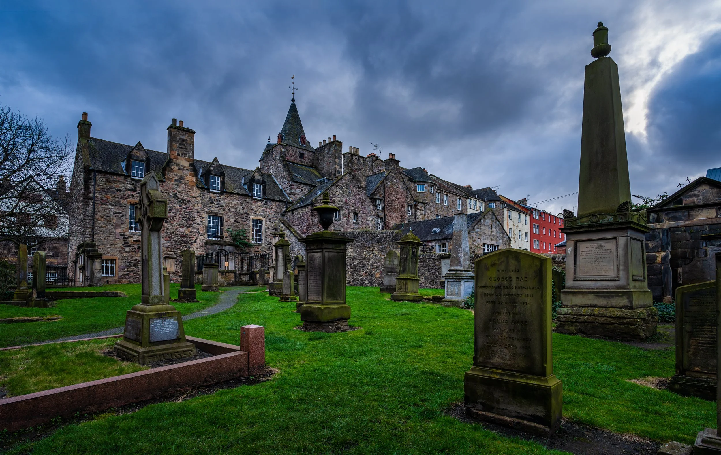 Historic gravestones at Greyfriars Kirkyard in Edinburgh, Scotland, surrounded by centuries-old stone architecture beneath a dramatic cloudy sky.