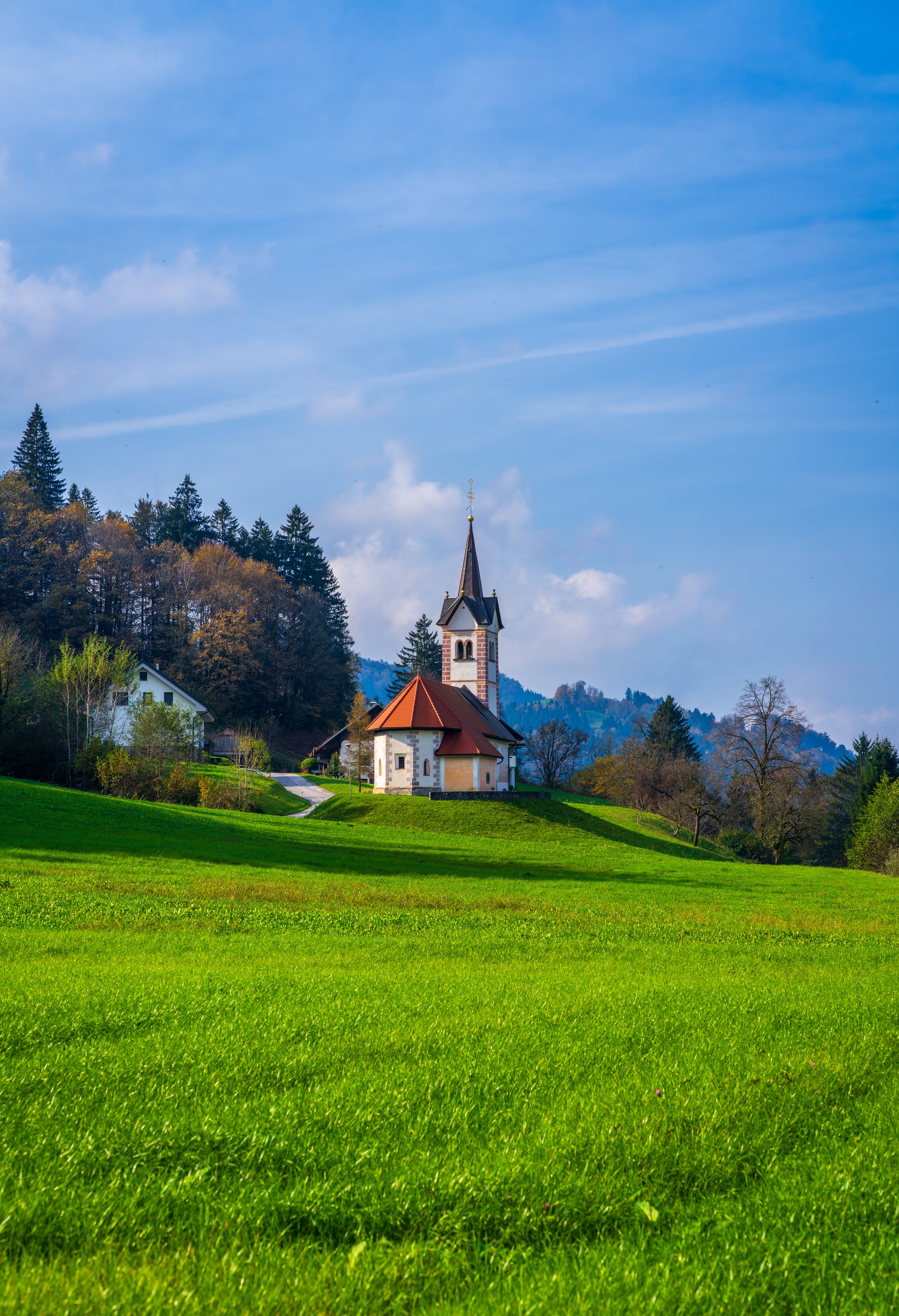 Charming countryside church with red roof and mountain backdrop in Upper Carniola, Slovenia - a hidden gem for travelers exploring rural landscapes and photography spots.