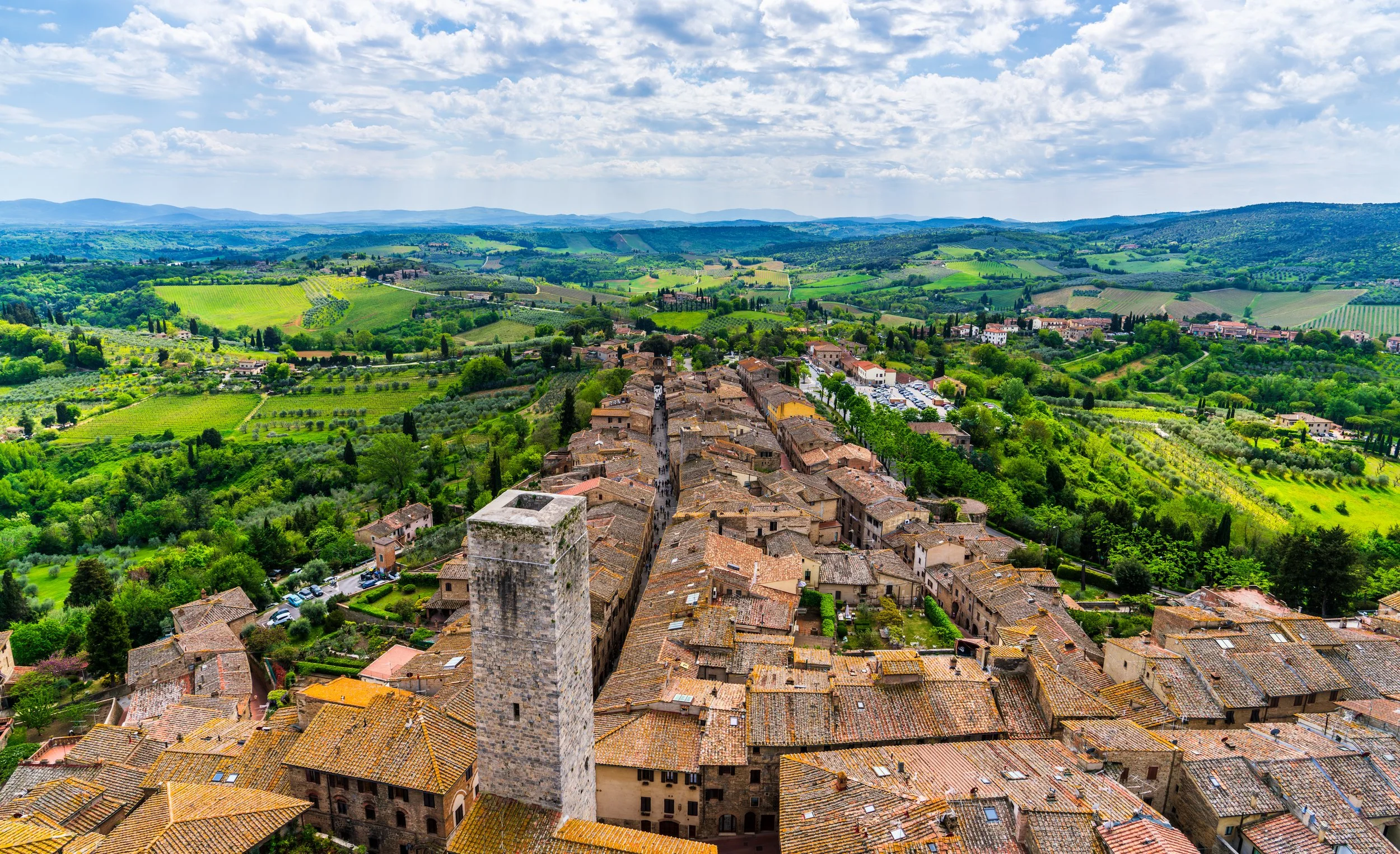 A panoramic view of the UNESCO World Heritage town of San Gimignano with its medieval rooftops, historic towers, and the rolling vineyards and olive groves of the Tuscan countryside. Fine art travel and landscape photography capturing one of Italy's 