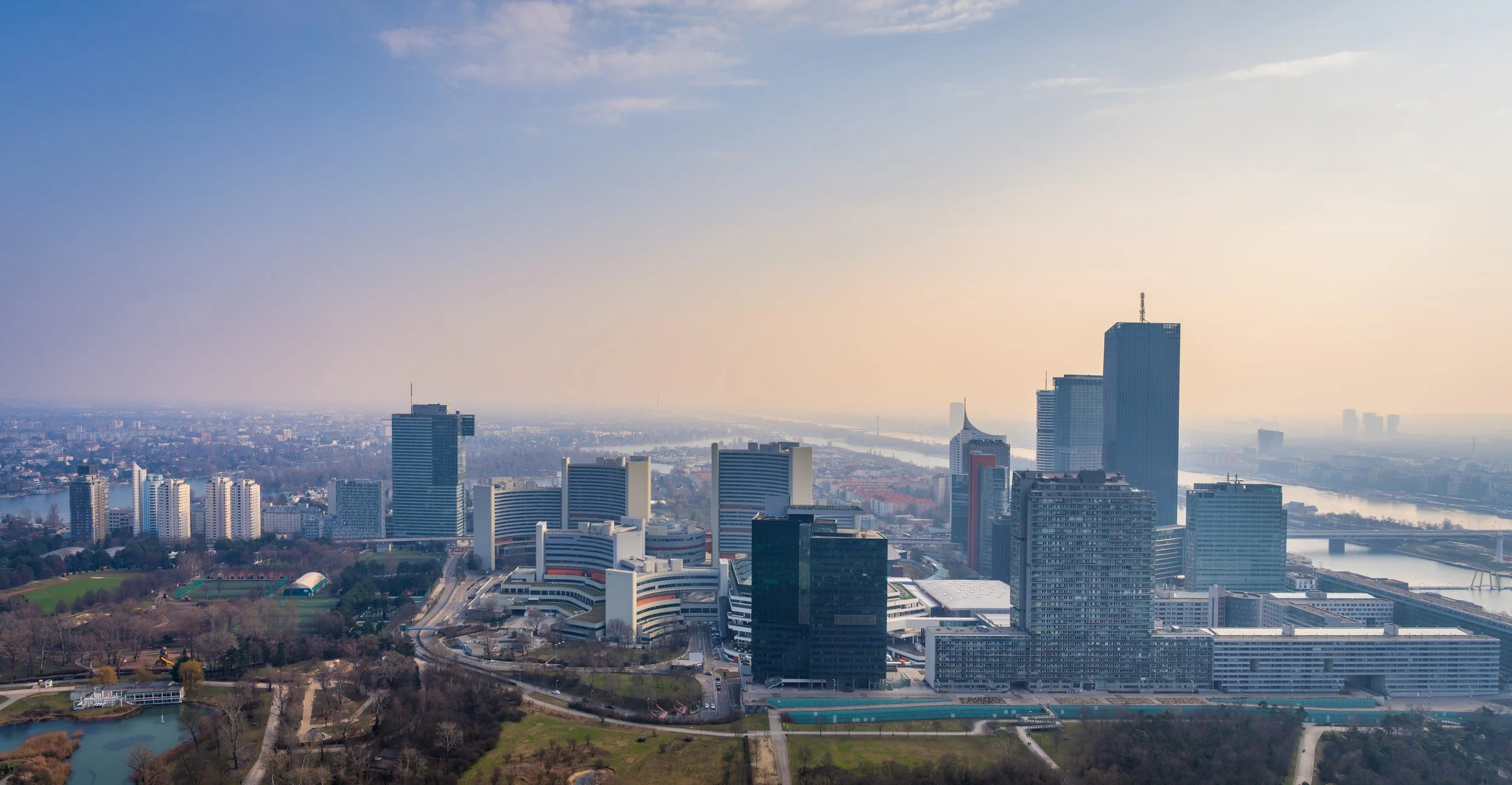 A modern travel photography cityscape of Vienna, Austria, featuring the skyline of Donau City with contemporary skyscrapers along the Danube River. Captured in soft atmospheric light, the image highlights the contrast between urban architecture and s