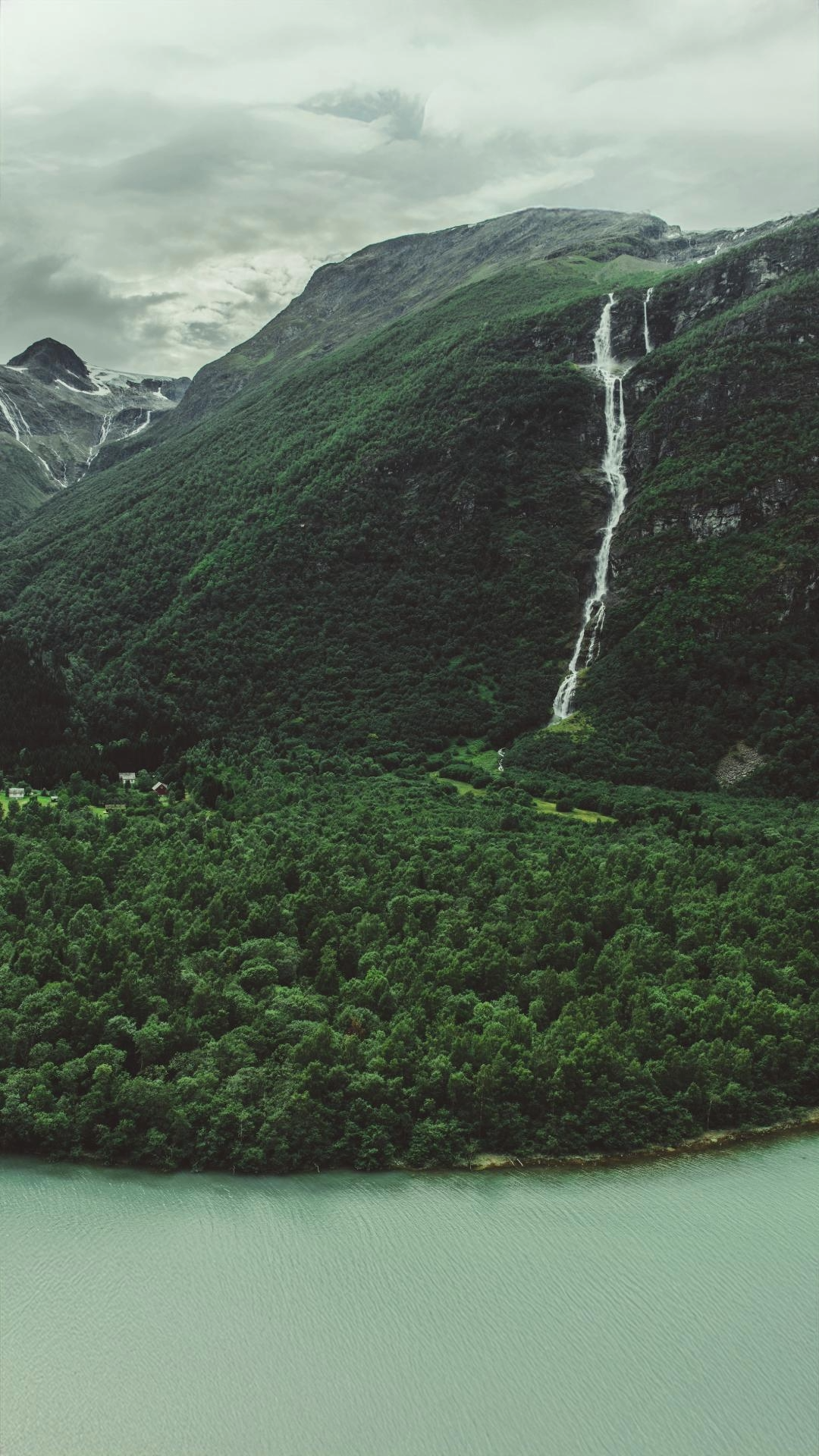 Green mountains with a waterfall cascading down the side, overlooking a body of water at the base.
