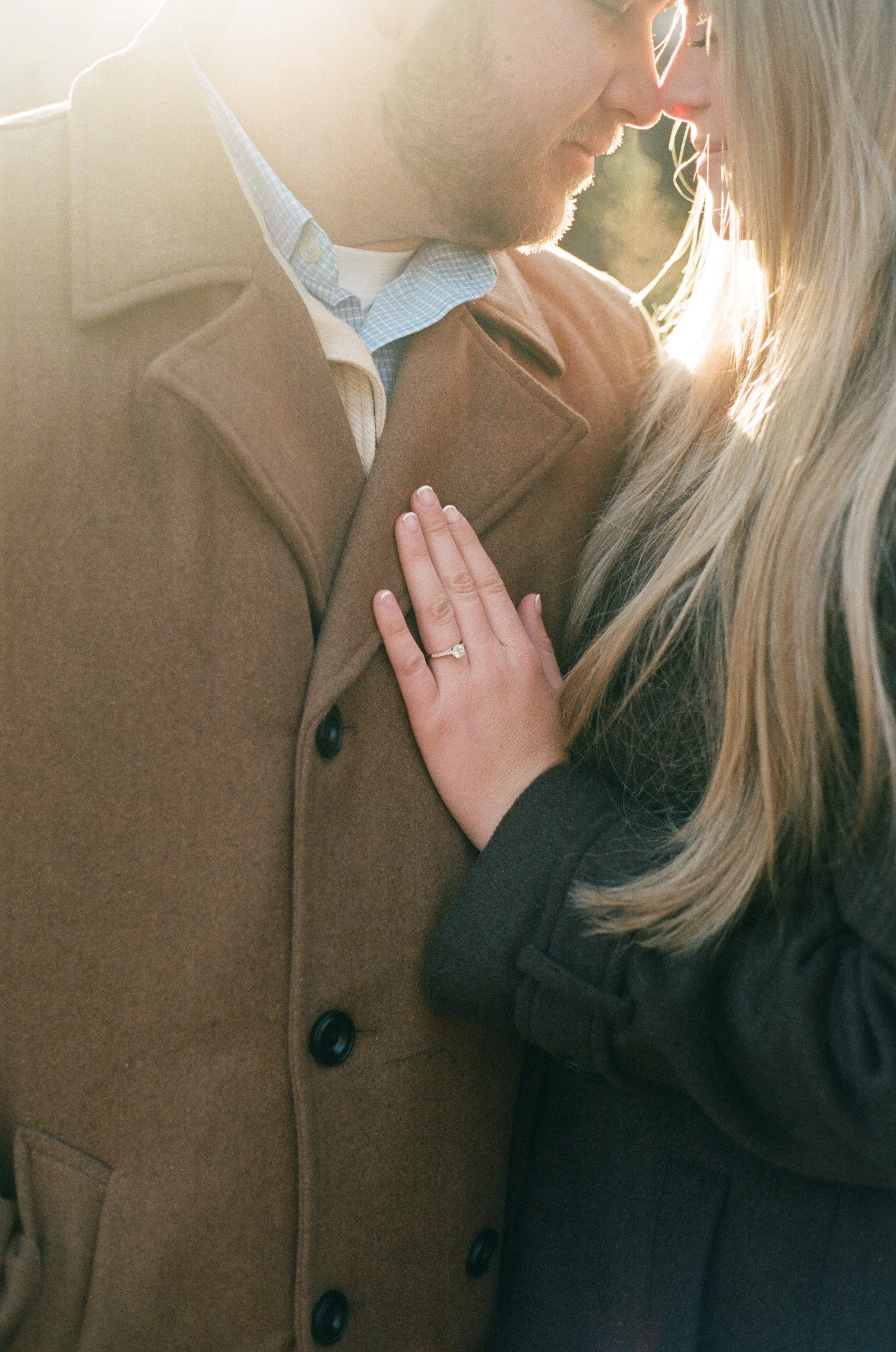 A man and woman close together, touching foreheads, with the woman's hand on the man's chest, showing an engagement ring.