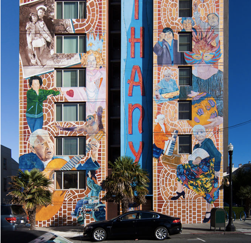 Colorful mural on a building with various people singing, playing instruments, and dancing, with a blue sky in the background and the word 'HAPPY' painted vertically in the center.
