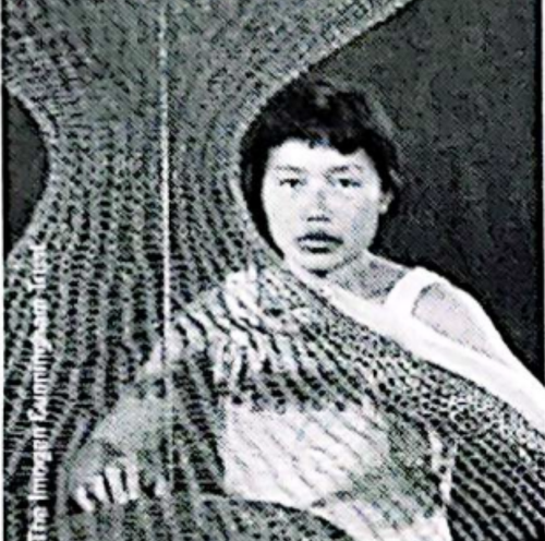 A black and white image of a young child with short hair, wearing a striped shirt, sitting with an arm resting on a surface.