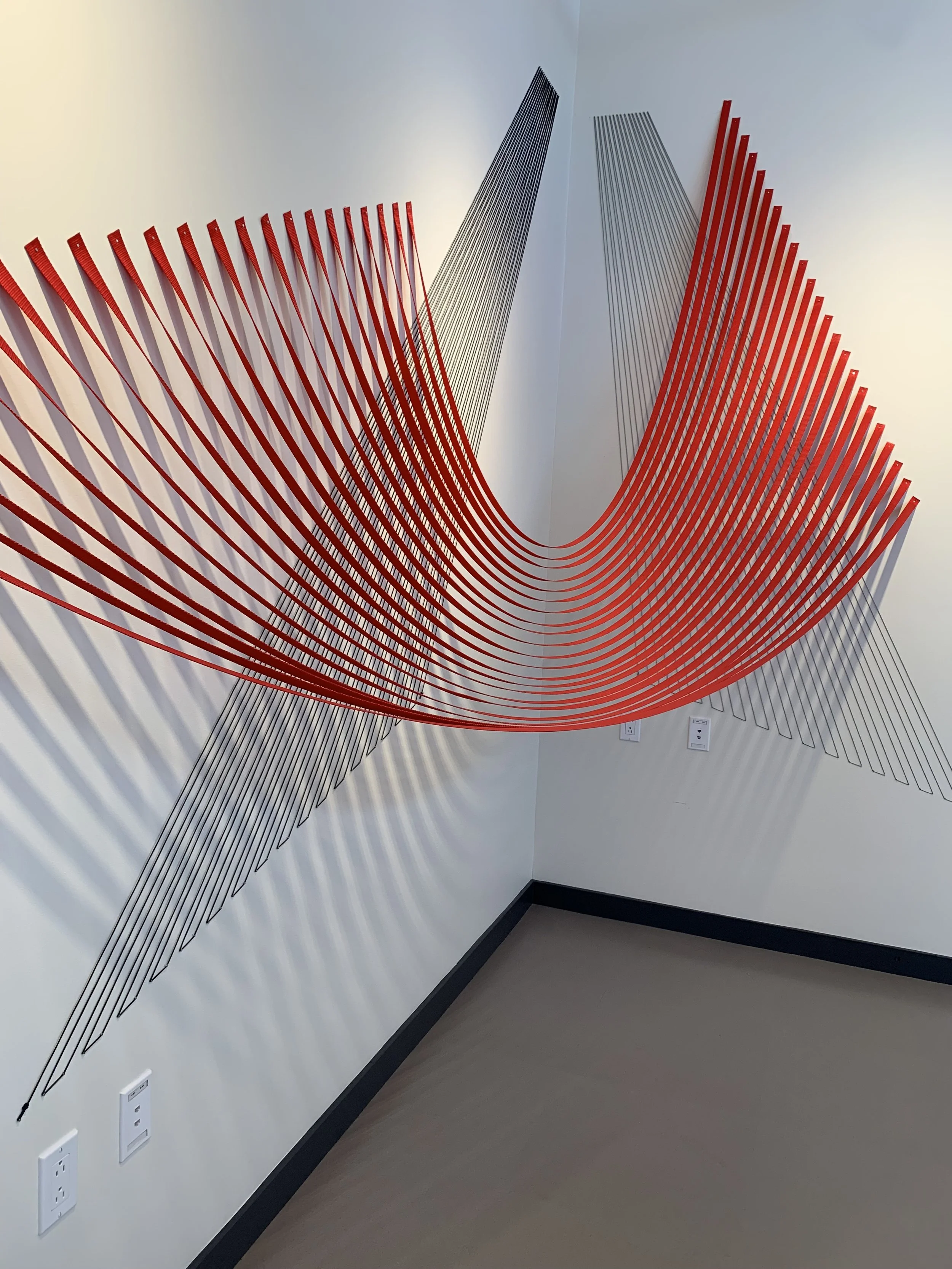 Wall art featuring a large, abstract sculpture with red and black wire elements, creating a flowing, wave-like pattern.