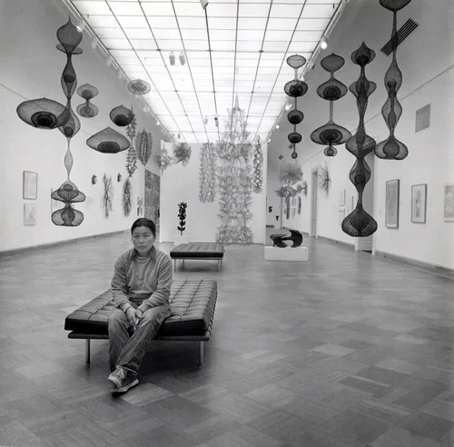A young boy sitting on a bench in an art gallery with hanging sculptures and artwork on the walls.