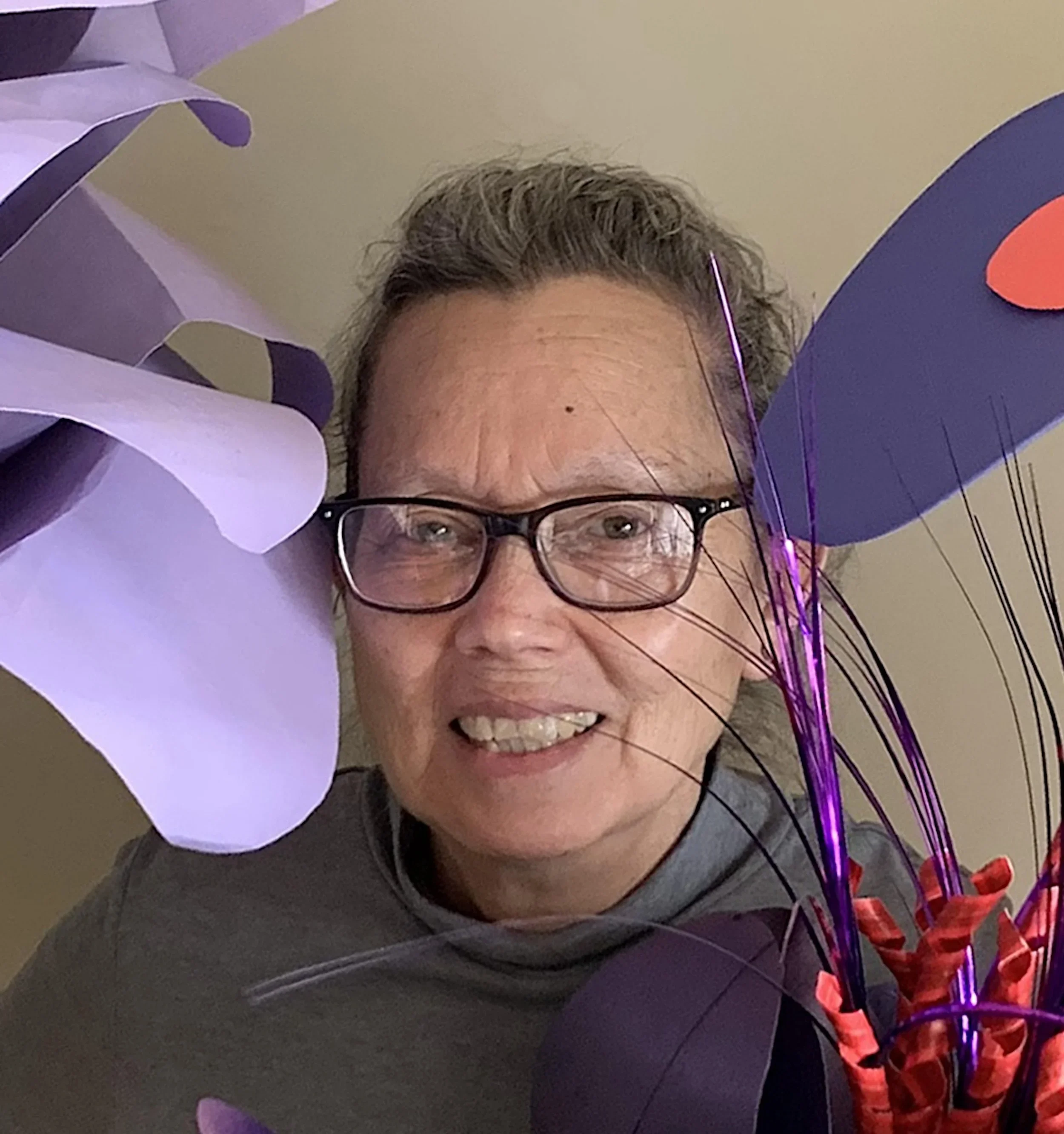 Close-up of a smiling woman with glasses surrounded by purple, pink, and red balloons.