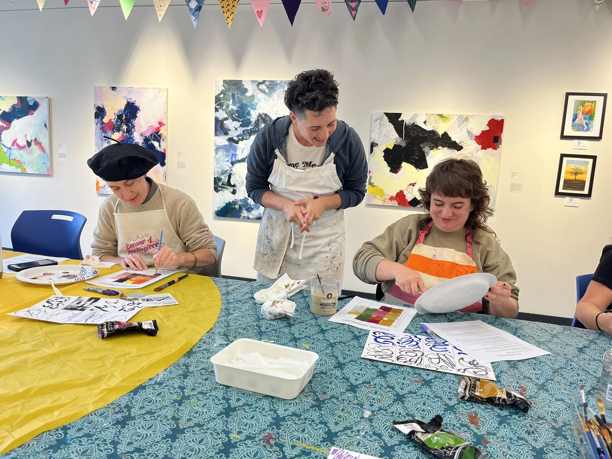 People painting and creating art in an art gallery, with colorful paintings on the walls and art supplies on the table.