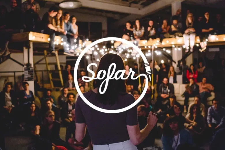 A woman stands on stage facing an audience in a dimly lit indoor venue, with people seated both on the main floor and a balcony, as the word 'SoFar' is overlaid in the center.