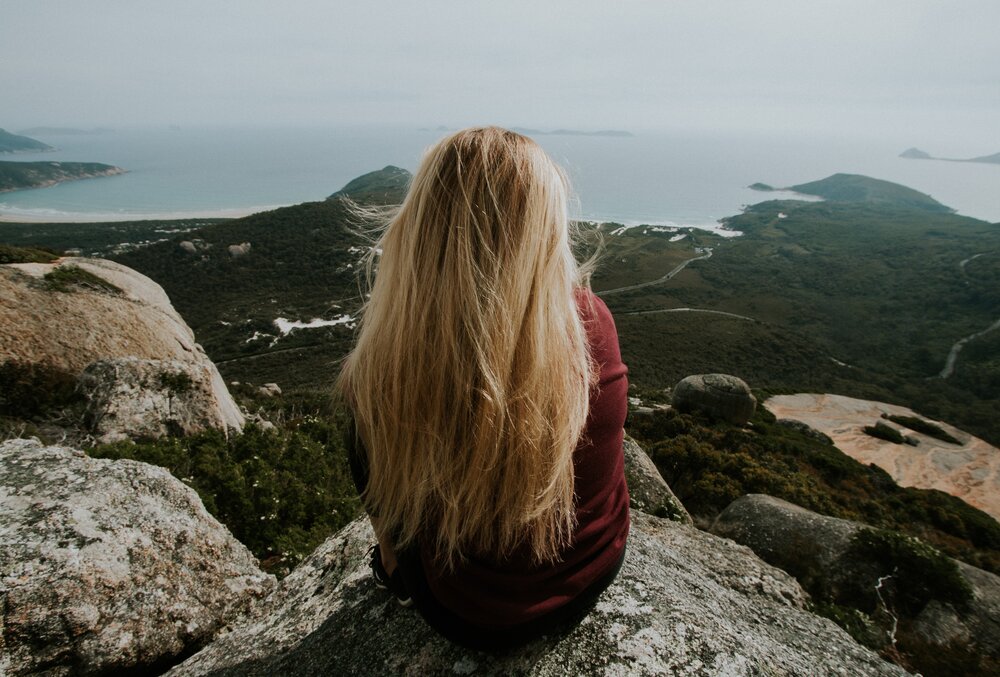 Stock picture of woman sitting alone on top of a mountain. Photo: Cody Board/Unsplash