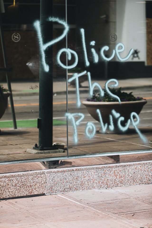 Graffiti on glass that reads 'Police The Police'. Photo: Logan Weaver/Unsplash
