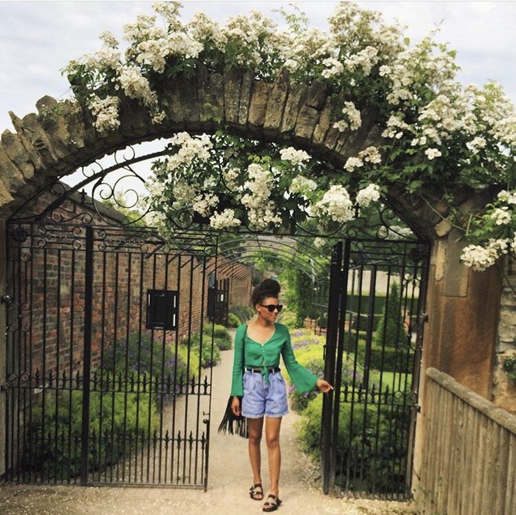 Evie in the archway of a beautiful brick door way, topped with white flowers. Photo: Evie Muir