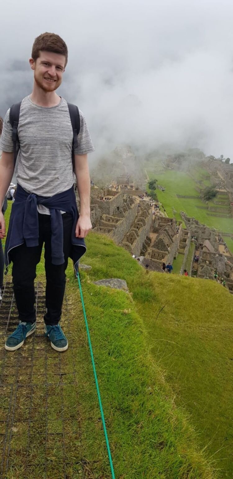 Alex hiking to Machu Picchu in 2019. He is standing so high up on a mossy step, there are clouds behind him at the same level. Photo: Alex Waite