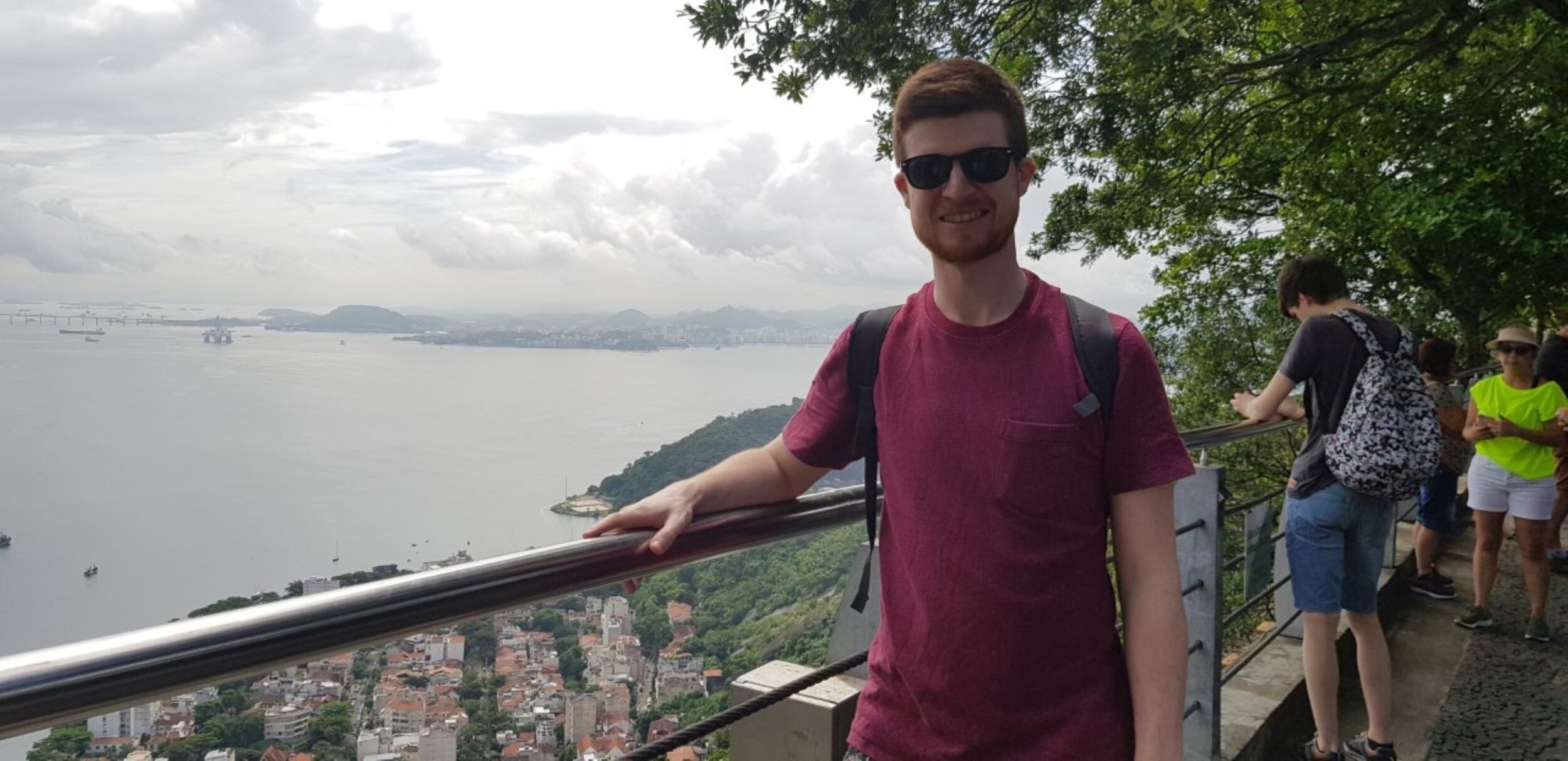 Alex travelling alone to Sugar Loaf Mountain 2019. He's standing with his arm on a glass balcony high up and a calm sea glistens in the background. Photo: Alex Waite