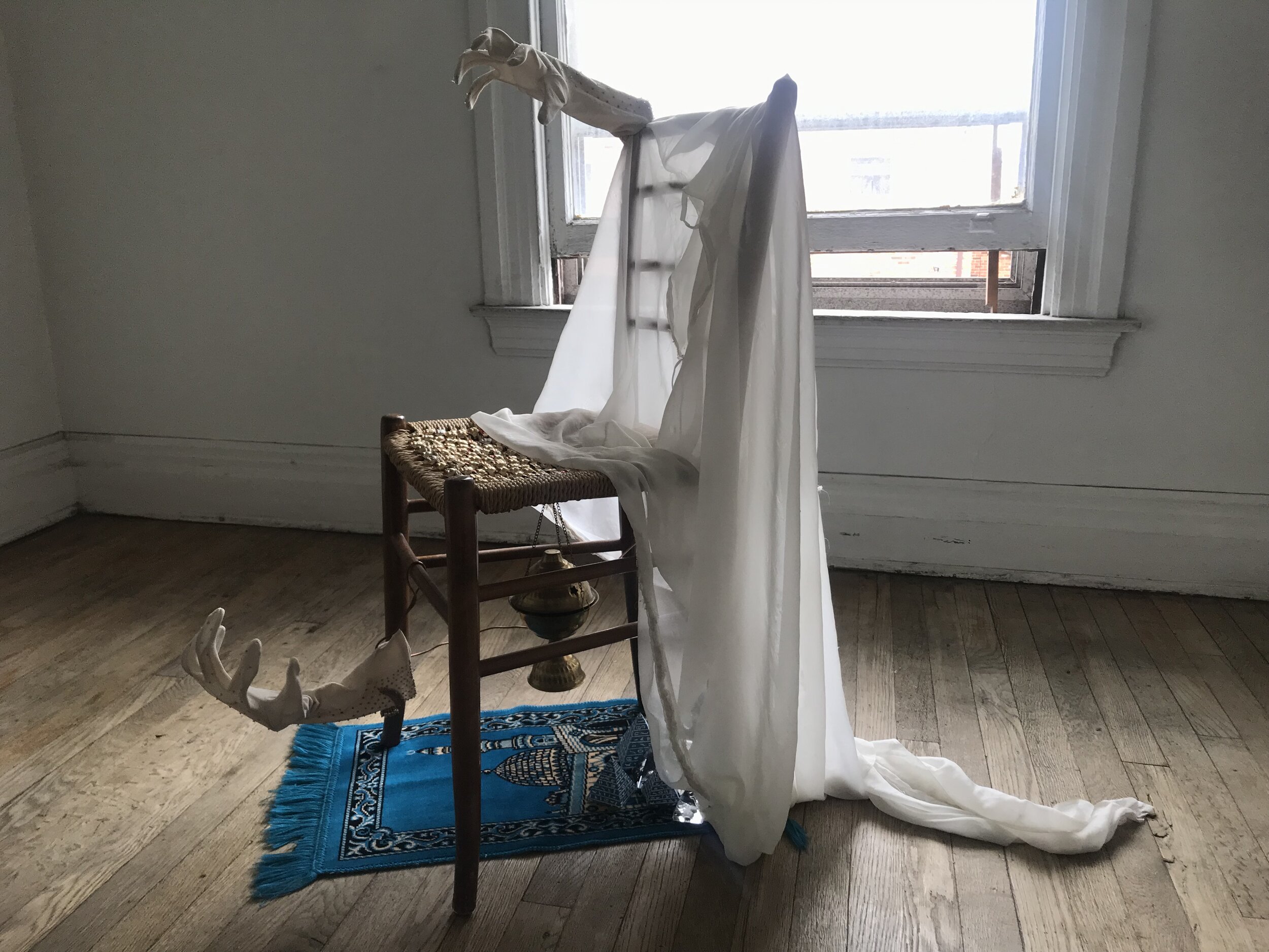   The Victim,  2019  chiffon prayer scarf,  wood and wicker chair, vintage hangers, embroidered gloves, prayer rug, vintage novelty rings, incense holder, copper wire, enamel, souvenir pyramids 