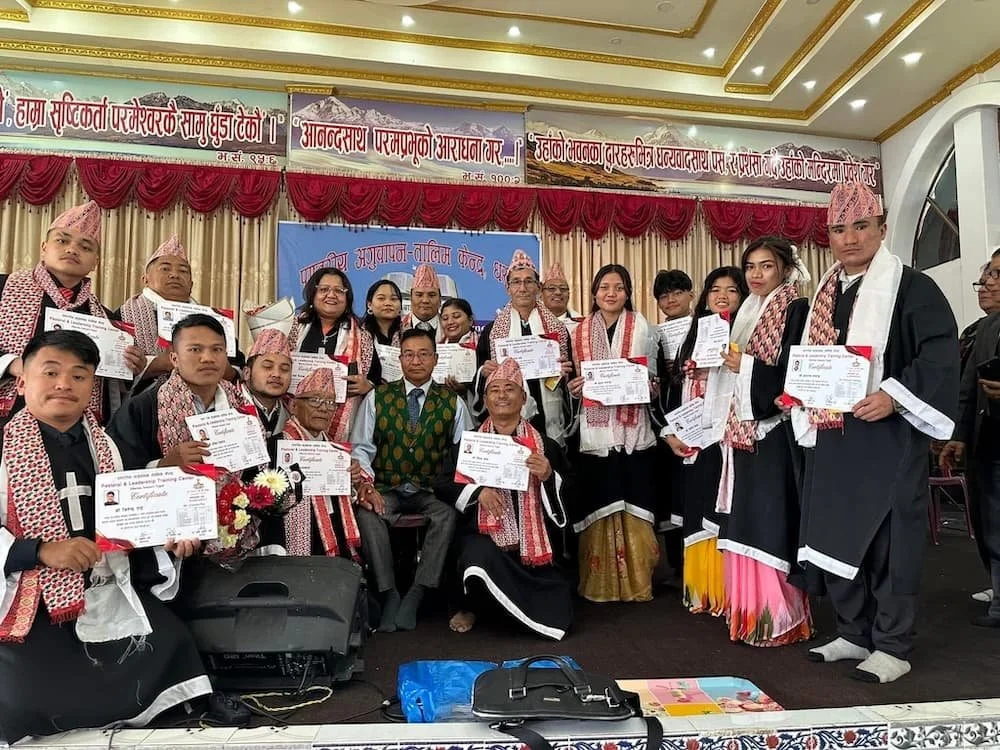 Group of people in traditional Nepali attire holding certificates, posing for a photo on stage during a graduation or certification ceremony.
