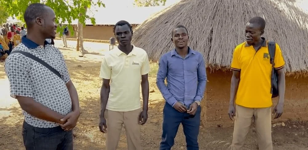 4 African theologians stand in front of a grass hut