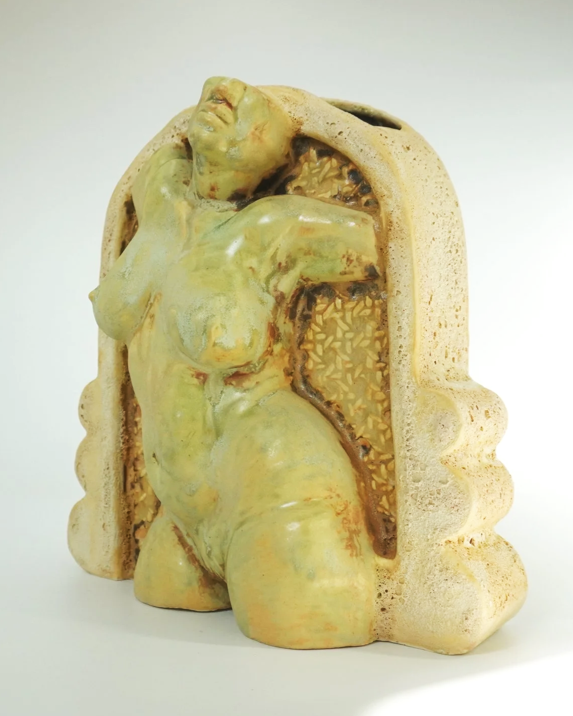 A ceramic figurative watertight vessel developed from an original sculpted form, slipcast and refined with handbuilt details. Several layers of glaze, oxides, cratered textured cathedral frames, and a caned webbing background behind the figure. Desig