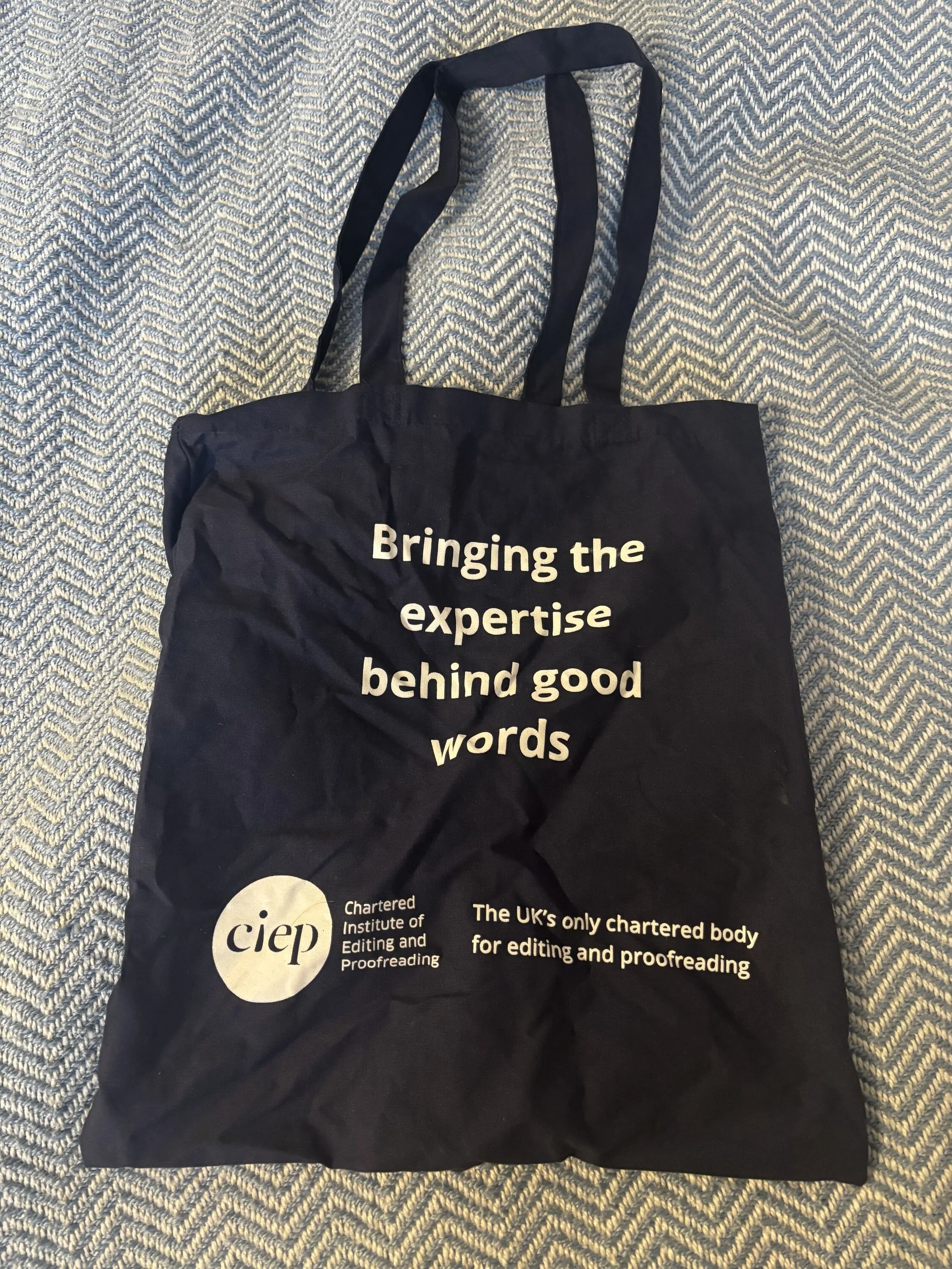 a photo of a navy tote bag with the words bringing the expertise behind good words and the logo of the chartered institute of editing and proofreading