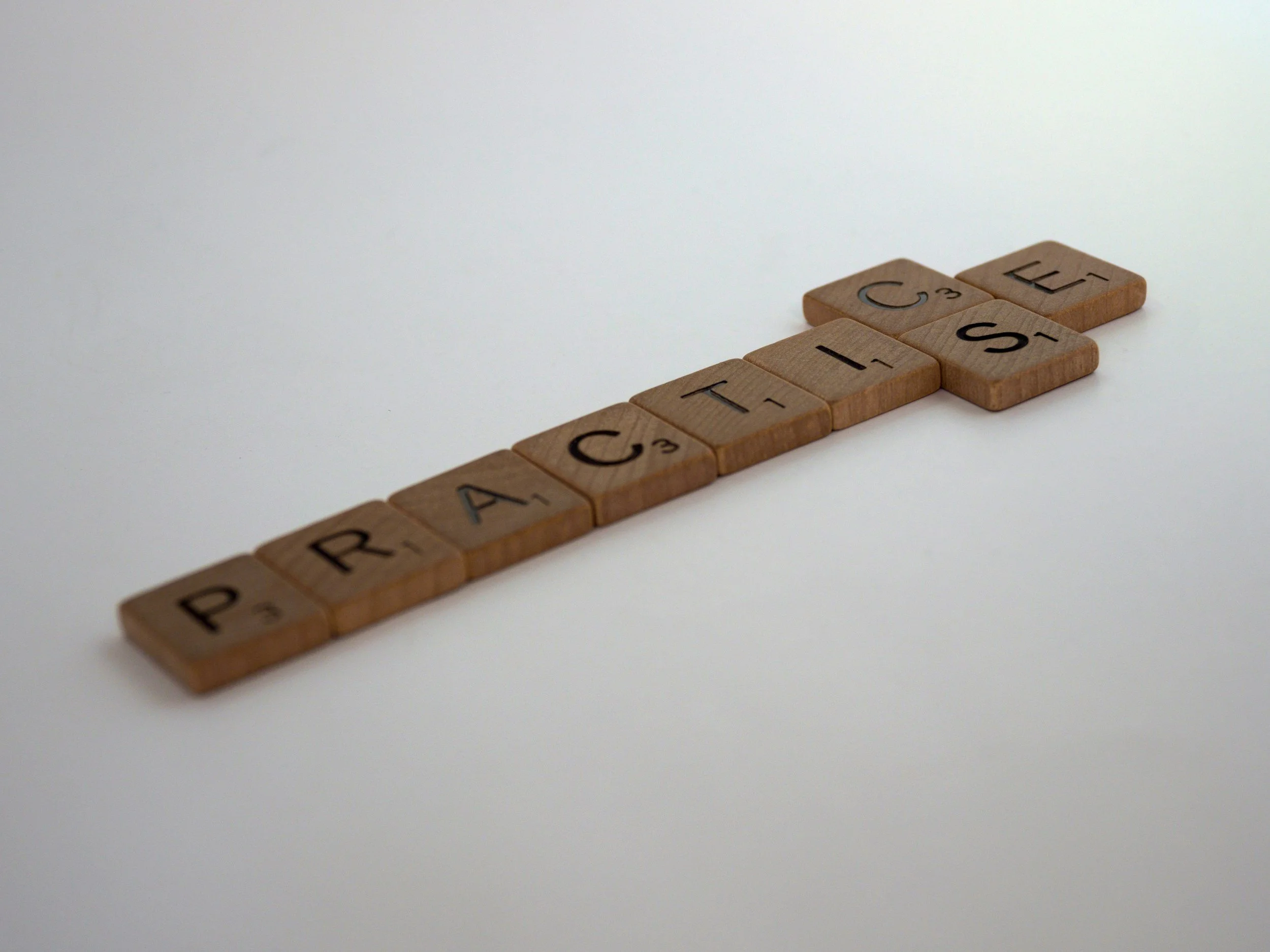 scrabble pieces assembled to make the word 'practice' with UK and US spelling variants