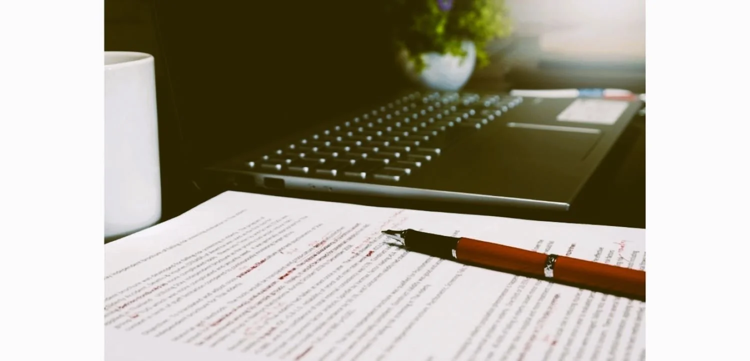 red pen on paper next to a laptop