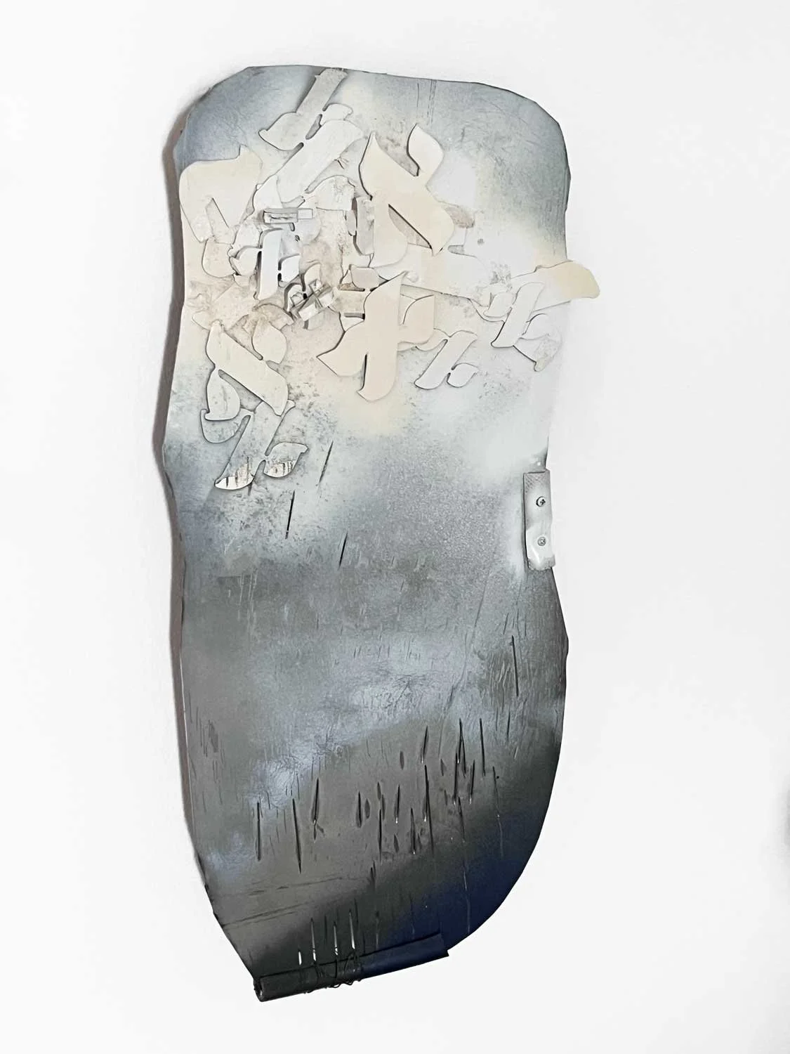 Wall-mounted aluminum sculpture with clustered white Hebrew letters rising from a weathered and scortched  metal surface, by Hodaya Louis