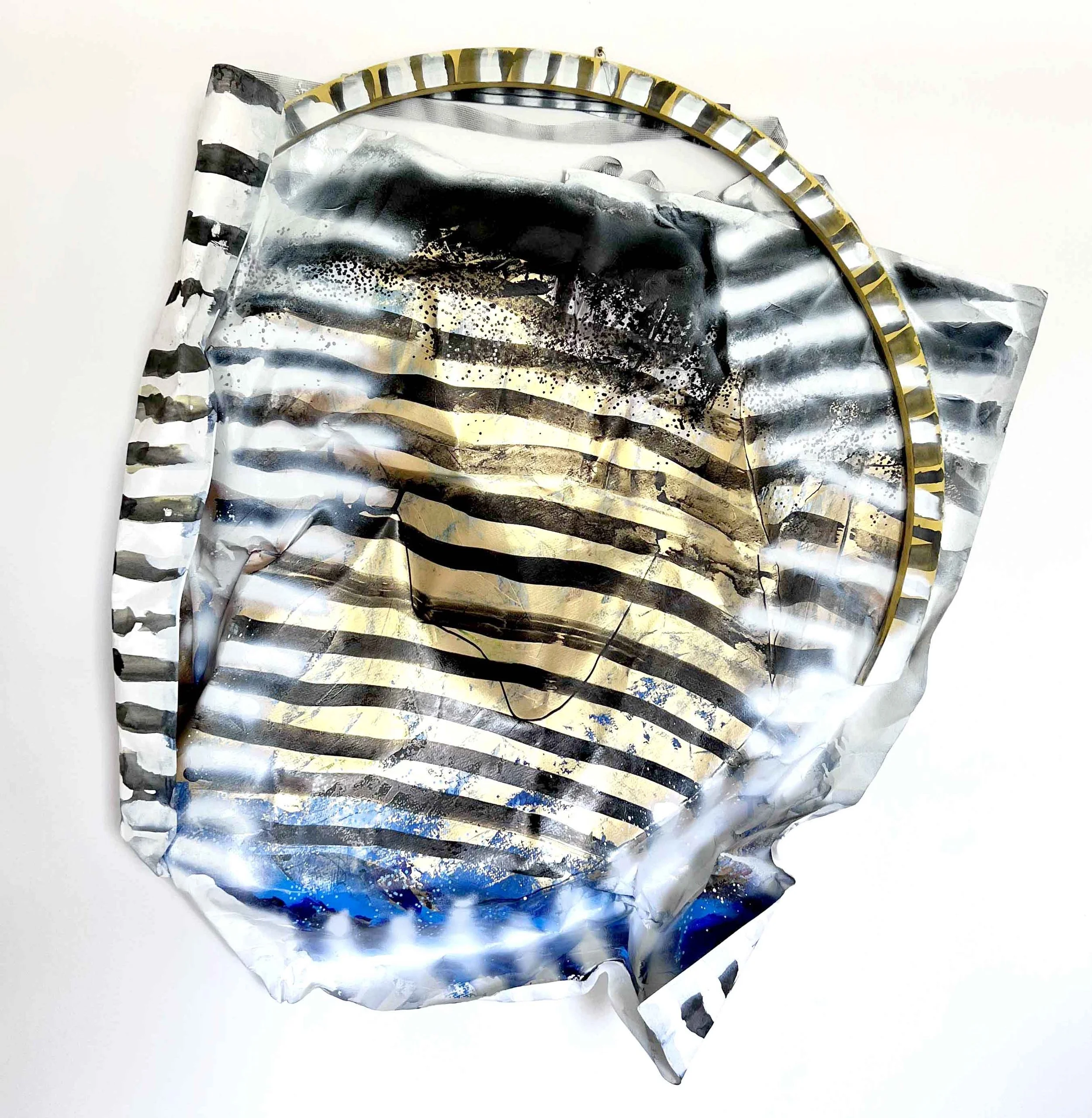Crumpled silver metallic foil with black and gold striped patterns, and a gold circular frame on a white background.
