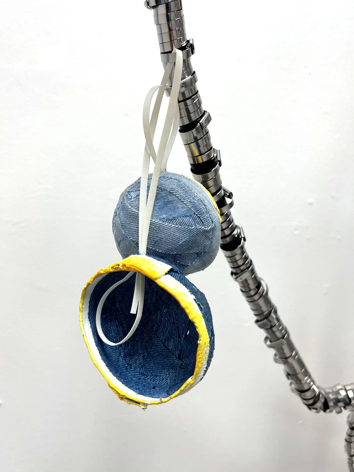 Circular aluminum sculpture with suspended blue denim fruit