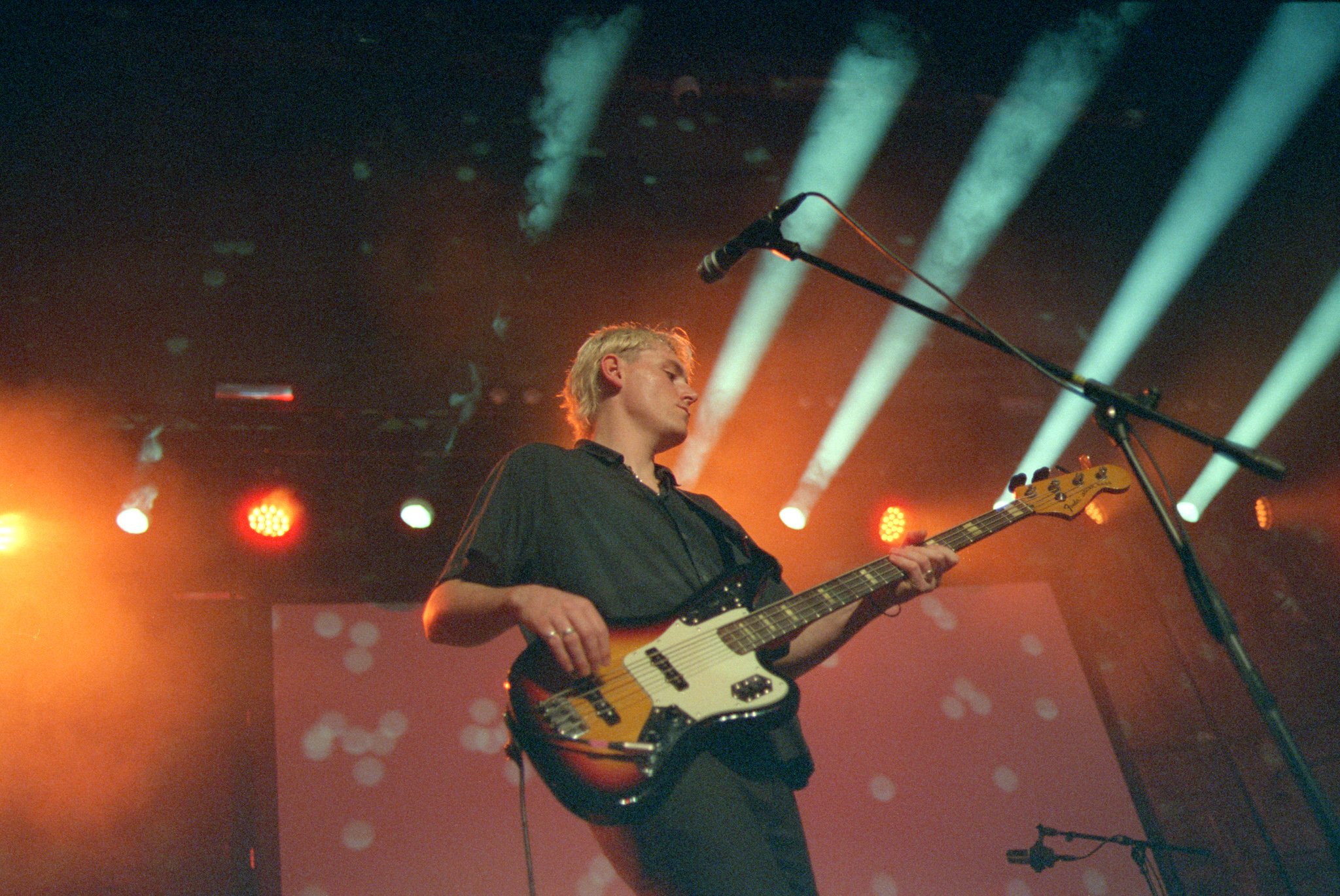 A musician with blond hair playing an electric bass guitar on stage under vibrant stage lighting. Boiler Shop Weddings Newcastle North East wedding band - book the best wedding band - the Gatenby's 