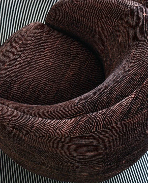 Close-up of a brown, textured, curved armchair with a striped background.