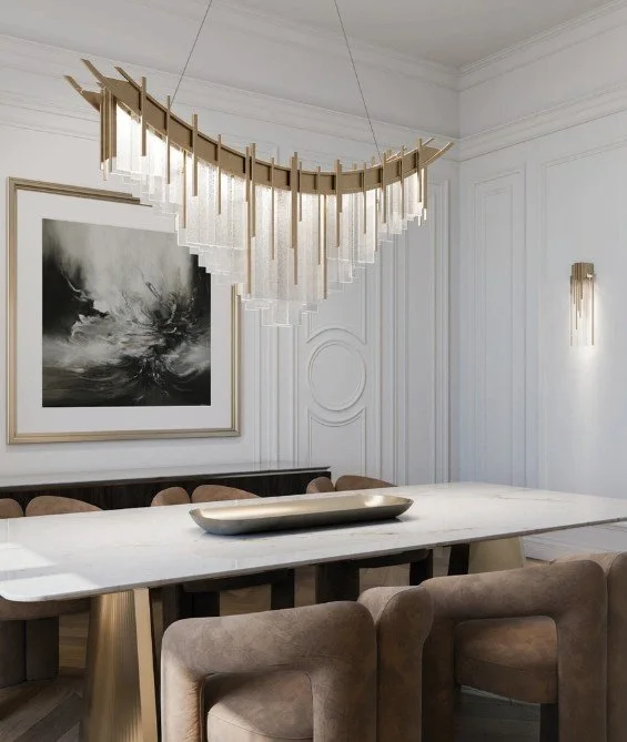Elegant dining room with a large marble table, beige upholstered chairs, modern chandelier with hanging glass rods, abstract black and white artwork, and white paneled walls with wall sconces.