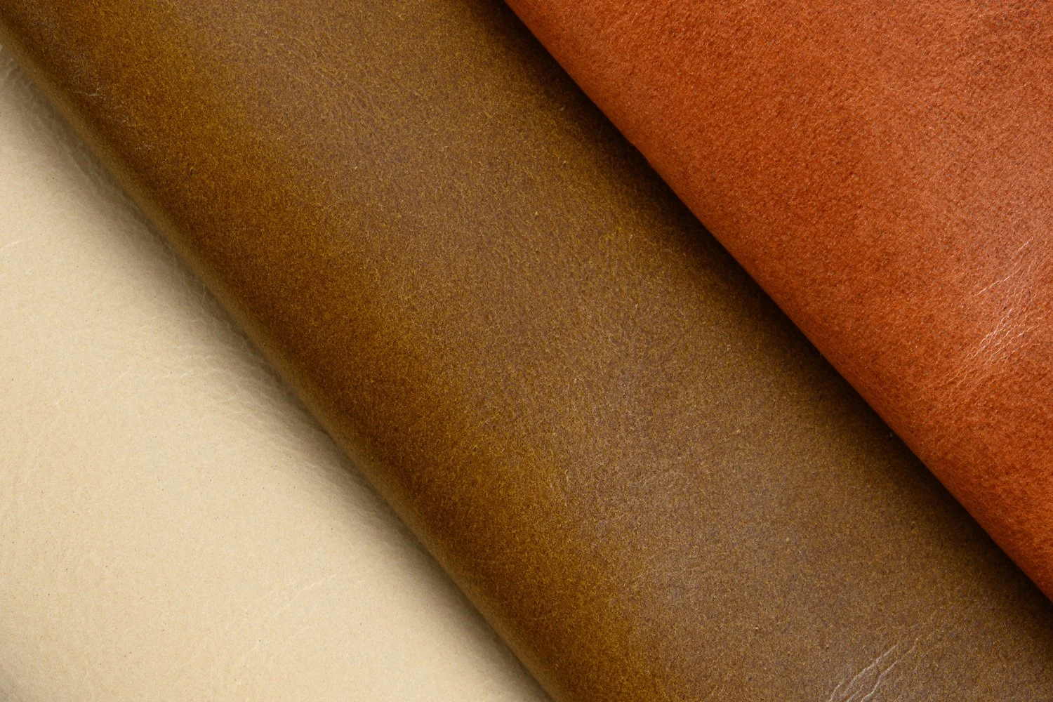 Close-up of three pieces of textured leather in beige, brown, and reddish-brown colors.