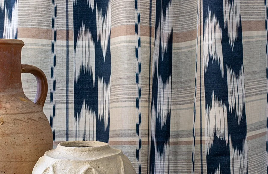 Three pottery vases of varying sizes and colors in front of a blue and white patterned curtain.
