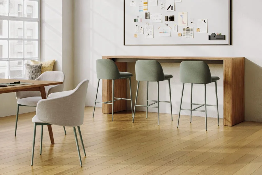 Modern interior with a large window, a white armchair, a dining table, and a wooden bar-height table with three green barstools in front of a white wall with an abstract art display.
