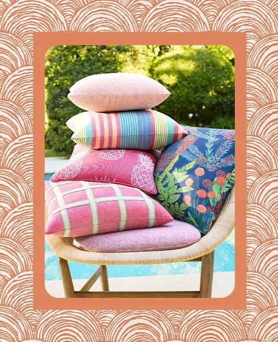 Stack of six colorful decorative pillows on a wooden chair outdoors with green trees in the background.