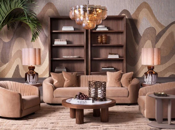 Living room with a beige sofa, two armchairs, a wooden coffee table, and a large dark wood bookshelf with decorative items. Two matching table lamps and a modern chandelier are also present.