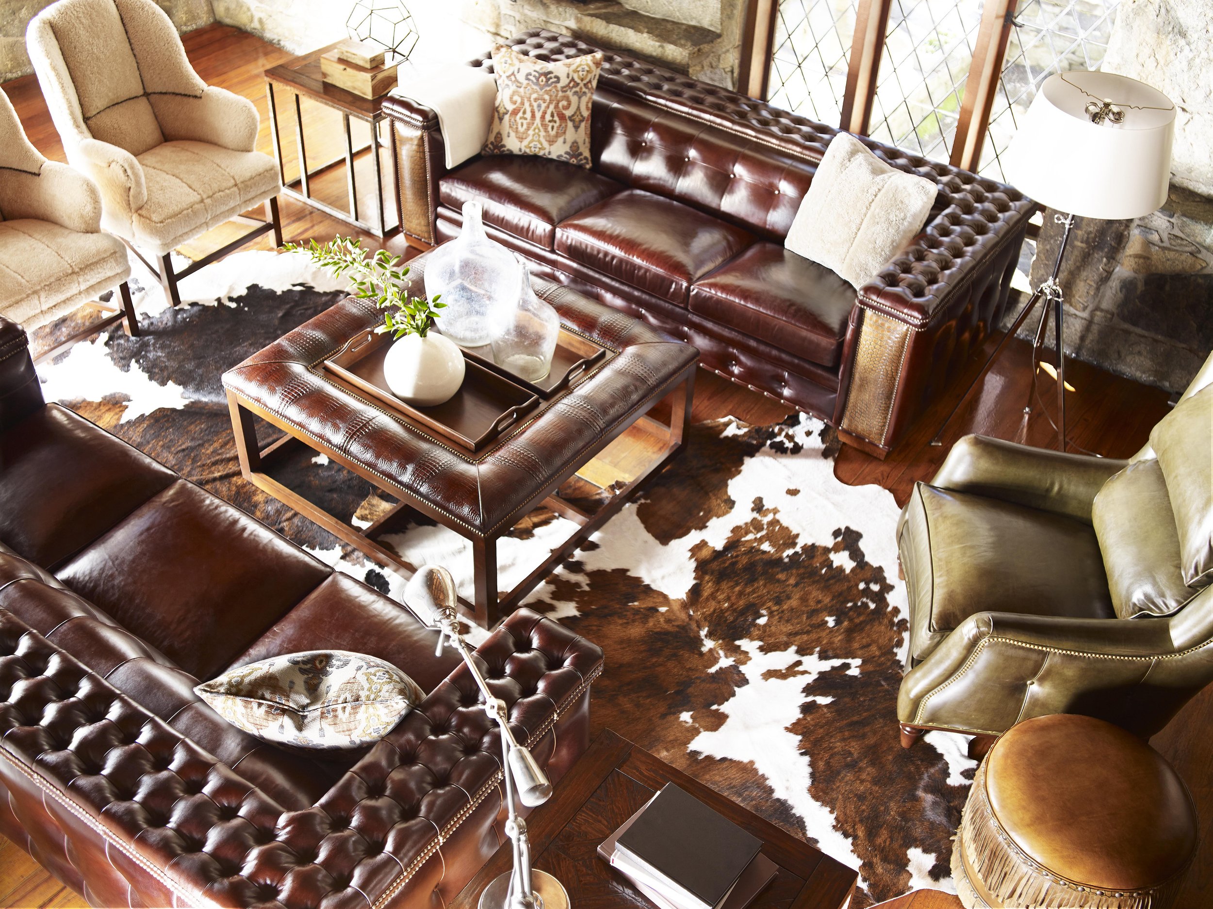 Living room with leather sofas, beige armchairs, a cowhide rug, a coffee table with decorative vases and a green plant, and a floor lamp with a white shade.
