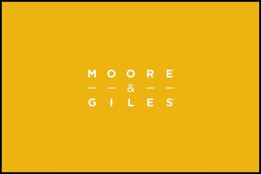 Yellow background with white text displaying 'MOORE & GILES' with stylized dashes.