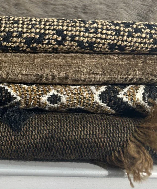 Stack of four folded carpets or rugs with different patterns and textures, a small part of brown fur or hair visible at the bottom right corner.