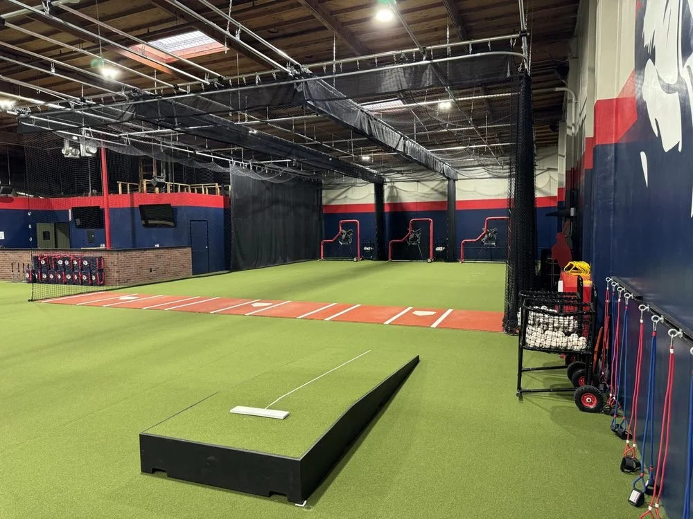 Interior photo of Mr Cages facility. We see out from the corner: 3 lanes of cages with netting removed so all a big space, plus some gear along the wall