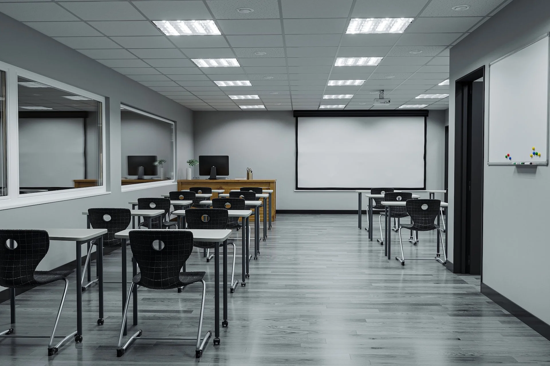 Classroom setup with projector screen, individual desks, whiteboard, and teacher workstation.