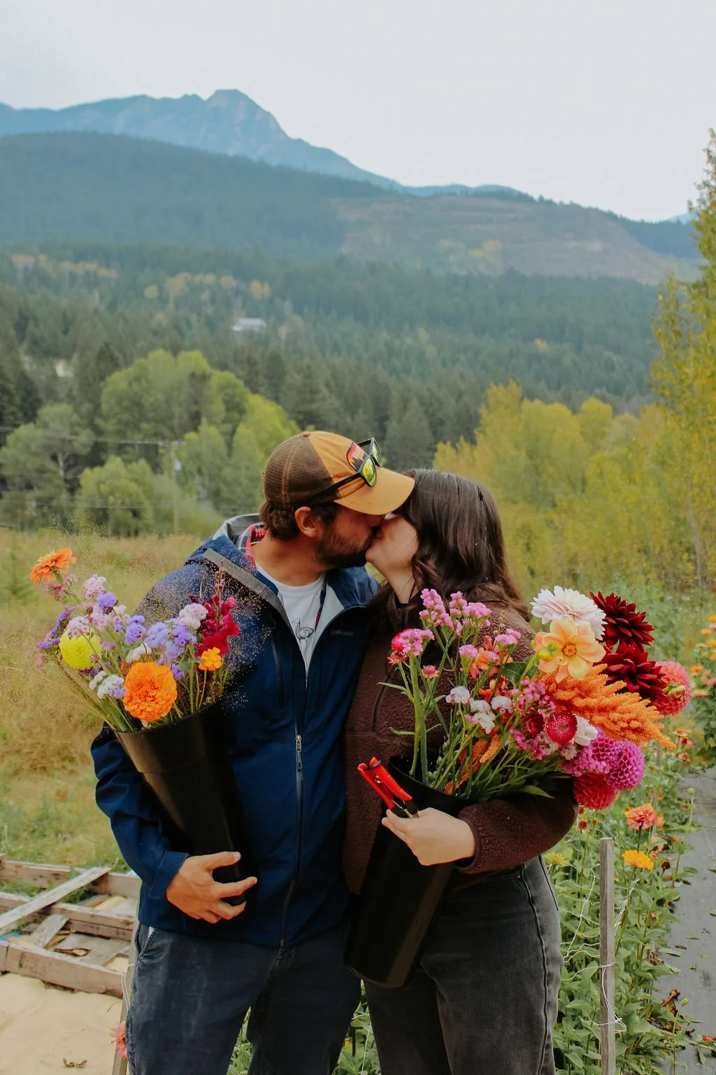 Two people kissing with armloads of flowers with mountains behind.jpg