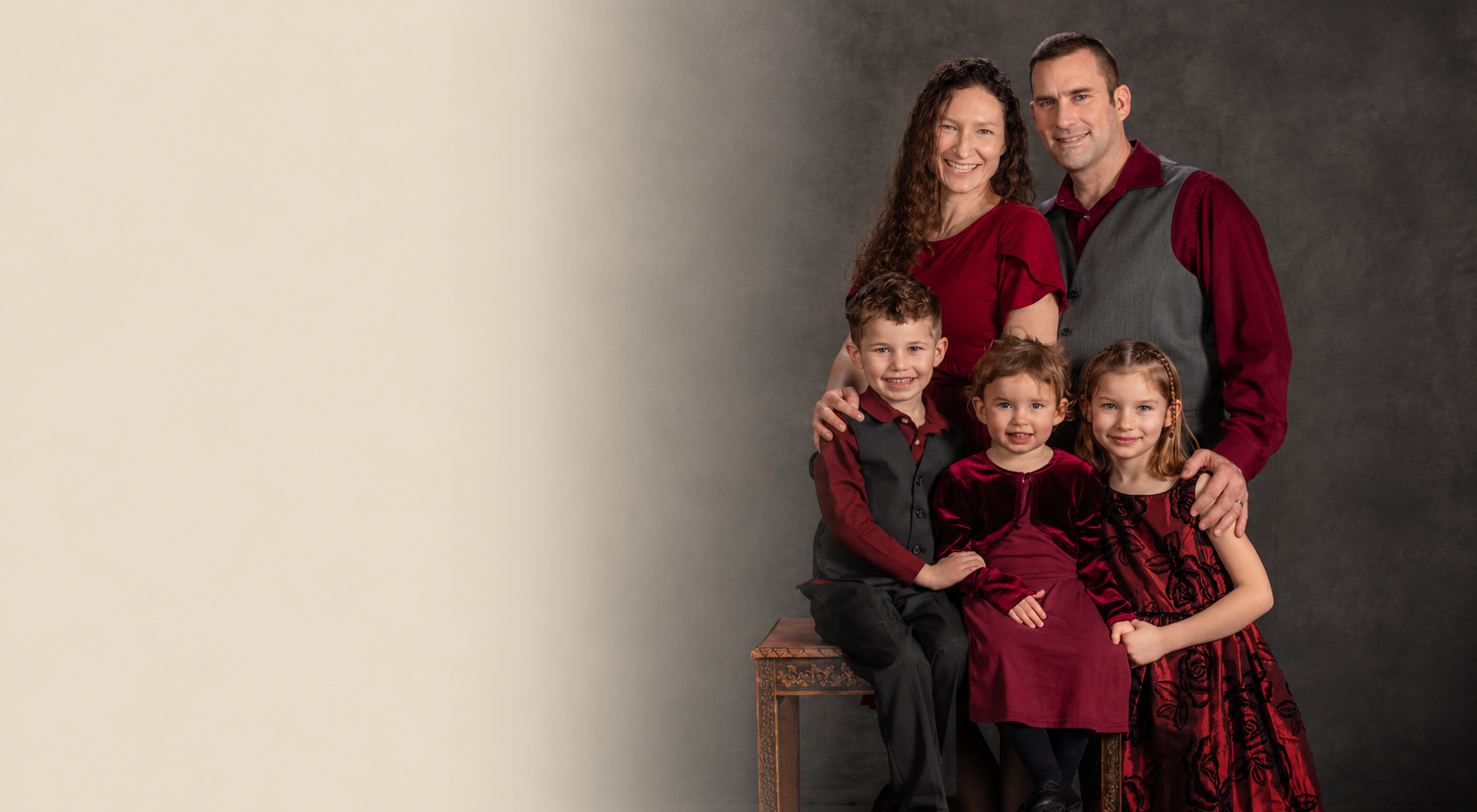 Fine art studio portrait of a family of five in coordinating burgundy and charcoal outfits against a classic painted backdrop